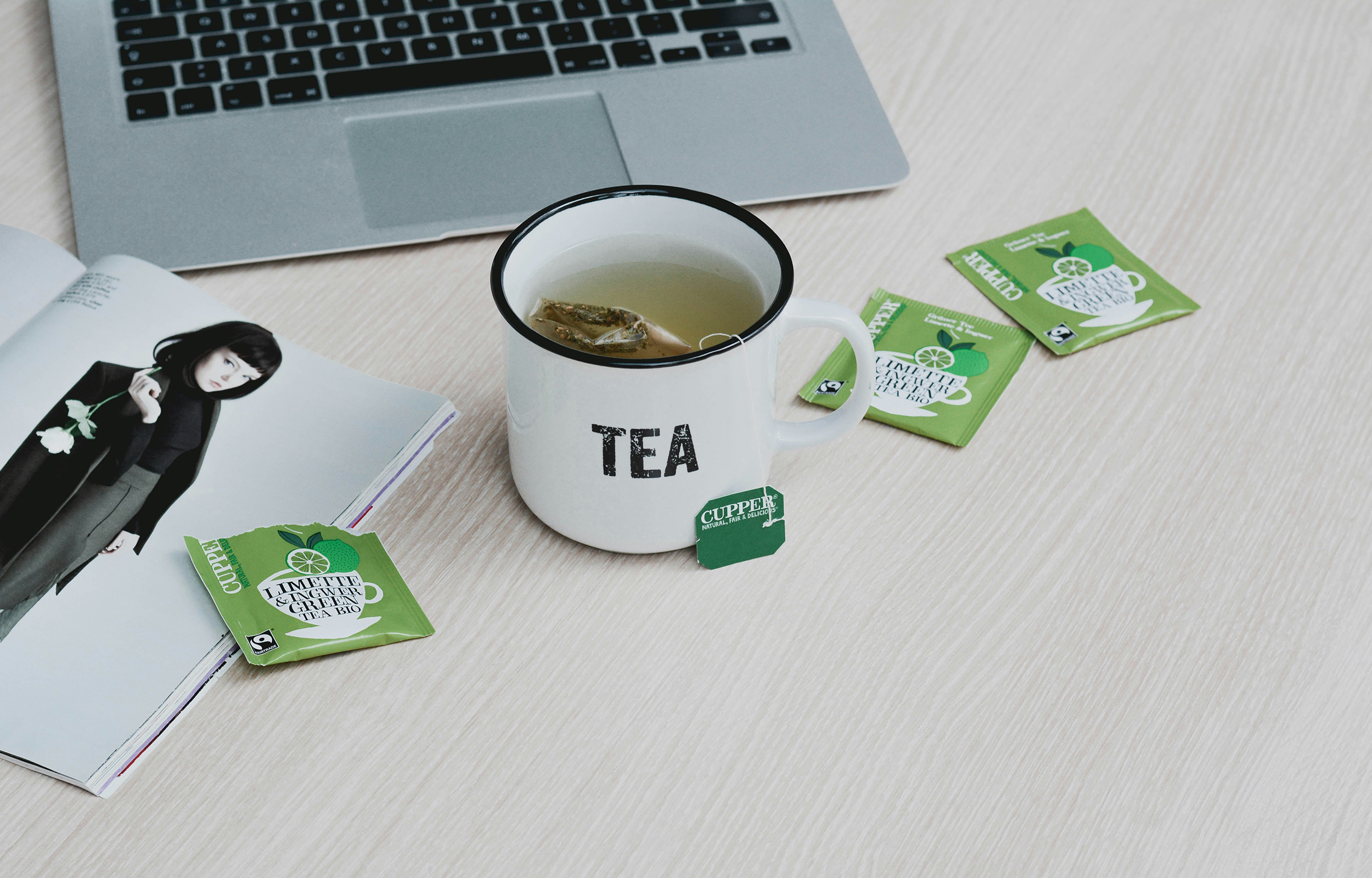 An image of a mug sitting by a laptop surrounded by teabag sachets